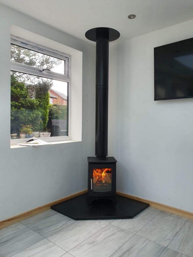 A lit corner stove resting on a custom-made pentagonal slate hearth