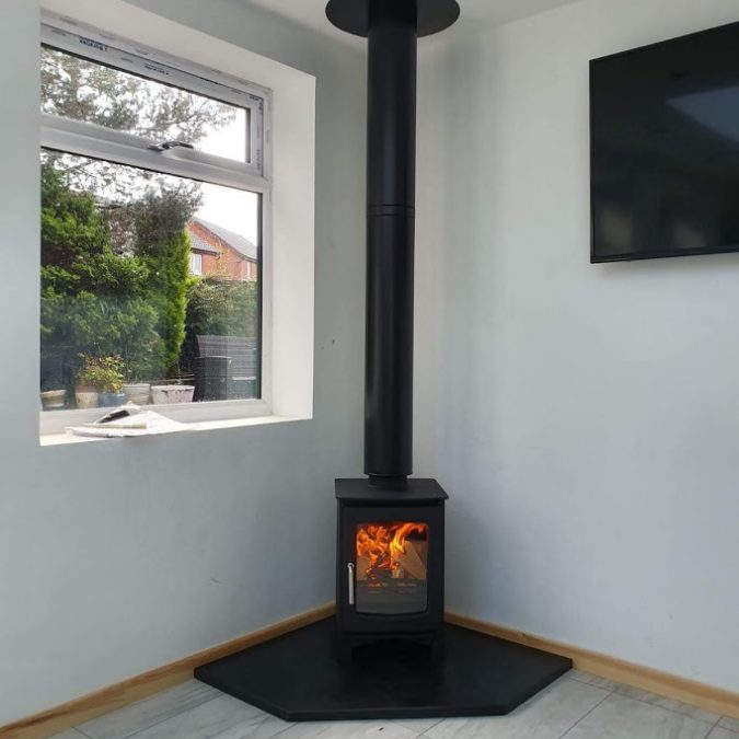 A lit corner stove resting on a custom-made pentagonal slate hearth