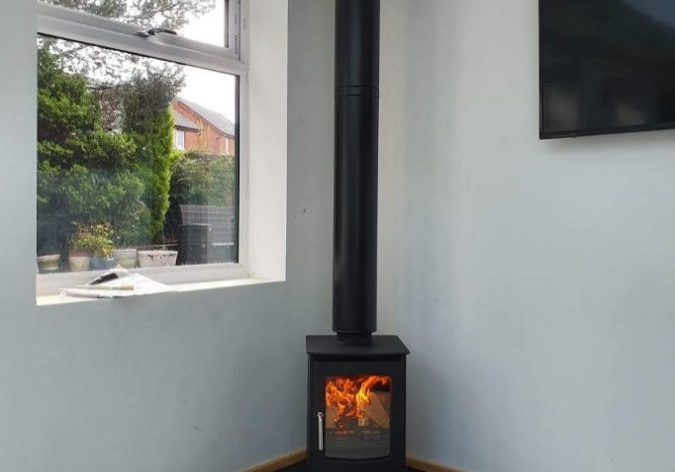 A lit corner stove resting on a custom-made pentagonal slate hearth